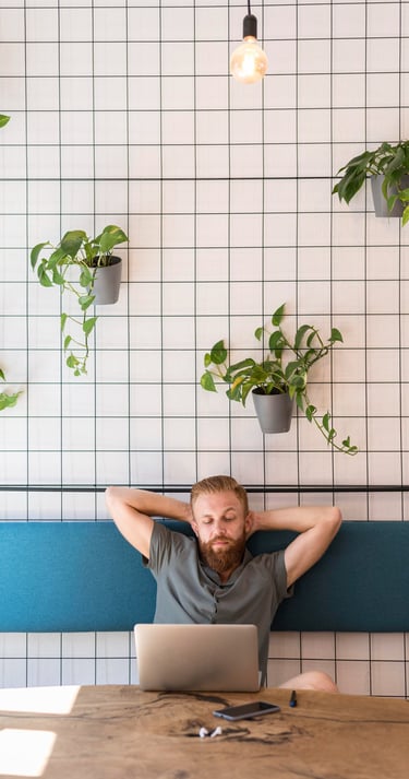 Persona tomando una pausa mental frente a su laptop en un espacio de trabajo con plantas