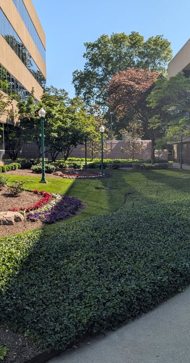 Professional office park courtyard with manicured landscaping, green hedges, and commercial buildings.