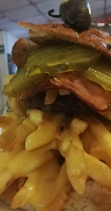 Hamburguesa gourmet con tocino, pepinillos y papas fritas crujientes bañadas en salsa de queso.