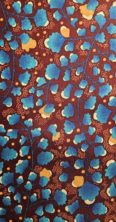 Floral African wax print fabric with blue leaf patterns and orange accents on a dark brown background.