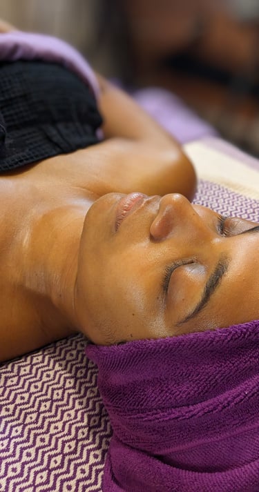 golden dark skin woman getting a facial at a spa with purple towels