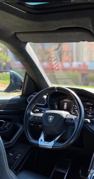 Interior view of a luxury Lamborghini Urus featuring a leather steering wheel and digital dashboard.