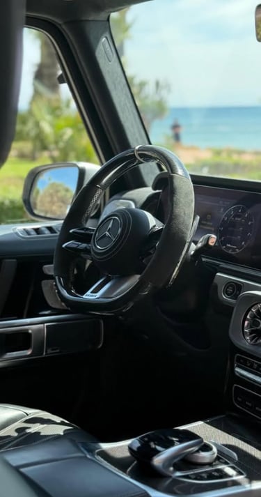 Luxury Mercedes-Benz G-Wagon interior with a carbon fiber steering wheel parked by the ocean.