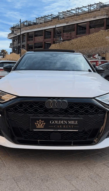 Front view of a white Audi luxury rental car parked on a cobblestone street at Golden Mile Car Rent.