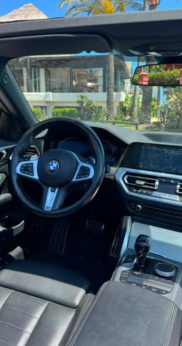 Interior view of a modern BMW convertible luxury car dashboard and steering wheel parked in a sunny tropical location.