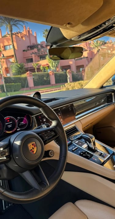 Luxury Porsche interior with tan leather seats and a digital dashboard parked near a coastal resort.