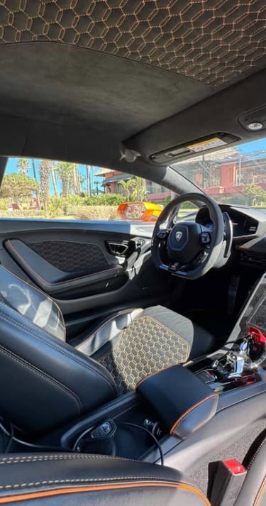 Luxury Lamborghini interior featuring black leather seats with orange honeycomb stitching and Alcantara trim.