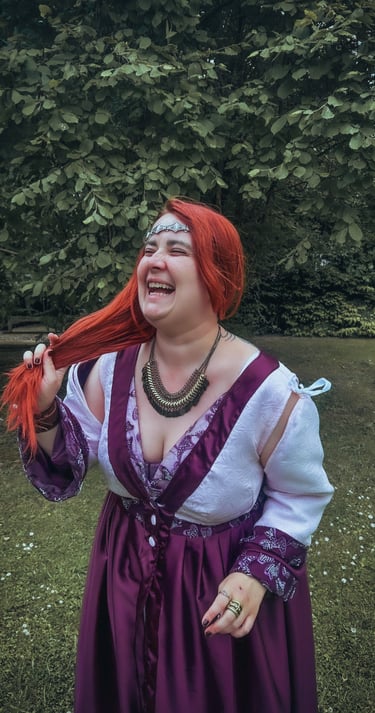Femme rousse riante et joyeuse dans une robe violette et blanche dans un fond verdoyant