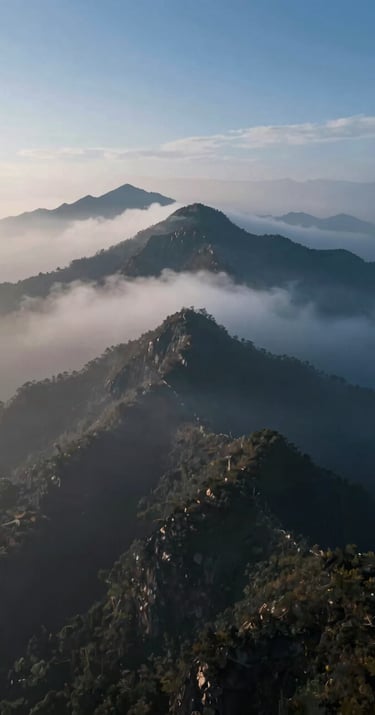 A breathtaking aerial drone shot of a misty mountain peak at dawn. Highly professional, dynamic mood. Incorporating #1B263B, #415A77, #A0B0C0, #E0E1DD.