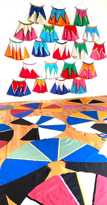 Handmade colorful circle skirts hanging on a wall and spread across a wooden floor in a sewing studio.
