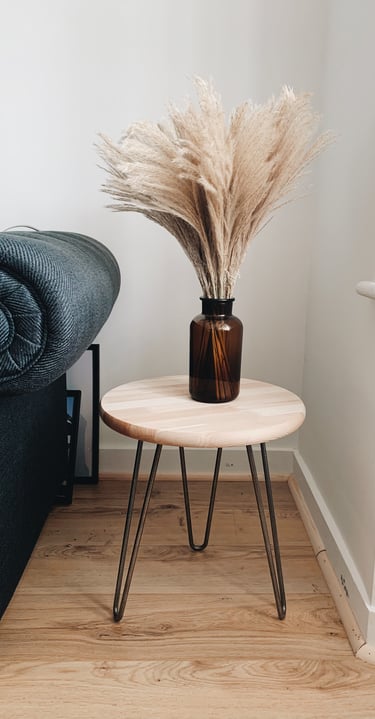 Detalle de decoración interior con mesa auxiliar de madera, jarrón con pampas y sofá oscuro.