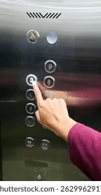 A hand pressing a glowing number three button on a stainless steel elevator control panel.