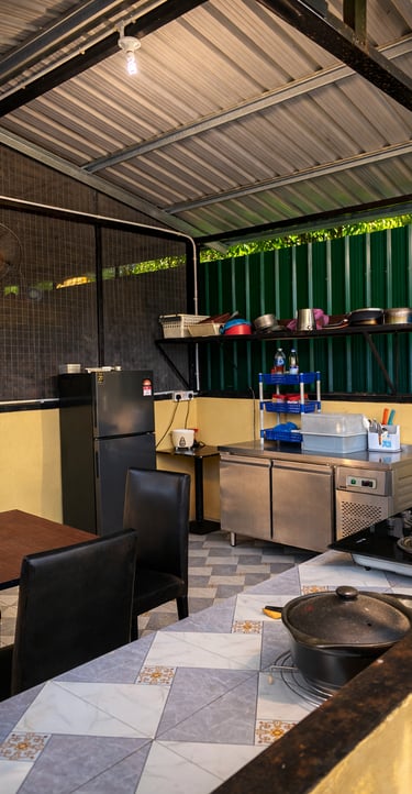 An outdoor commercial kitchen area featuring a stainless steel prep table, gas stove, and refrigerator.