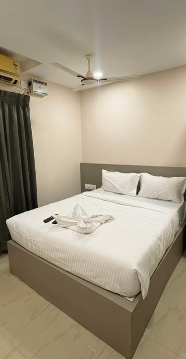 Modern budget hotel room with white double bed, gray wardrobe, air conditioning, and dark curtains.