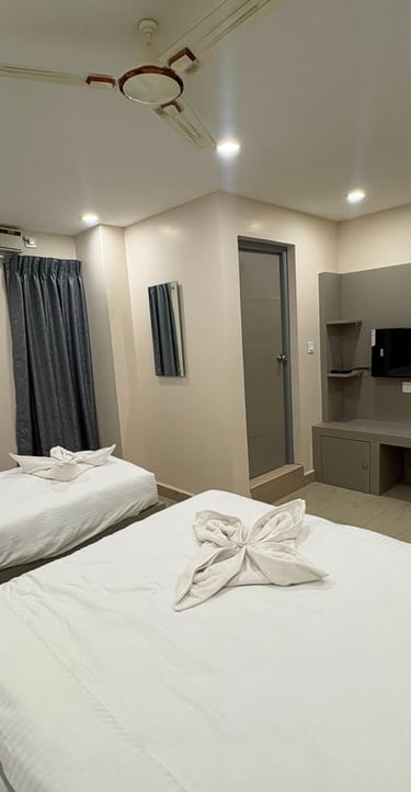 Modern hotel room with double and single beds, white linens, wall-mounted TV, and ceiling fan.