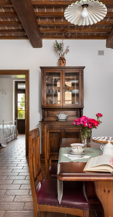 Rustic Italian kitchen and dining area featuring wooden ceiling beams, terracotta floors, and vintage furniture.