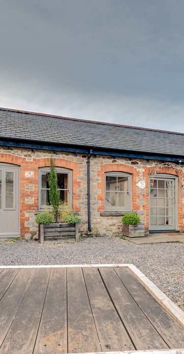 Stone cottage exterior with grey wooden doors and a rustic picnic bench on a gravel patio.