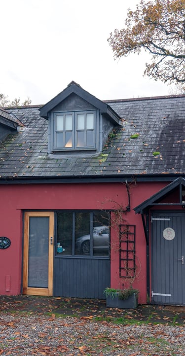 A charming red barn-style guesthouse with grey doors and dormer windows nestled among autumn trees.