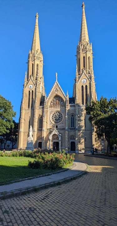 Gothic Revival St. Elizabeth Church with twin spires in a sunny Budapest park square.