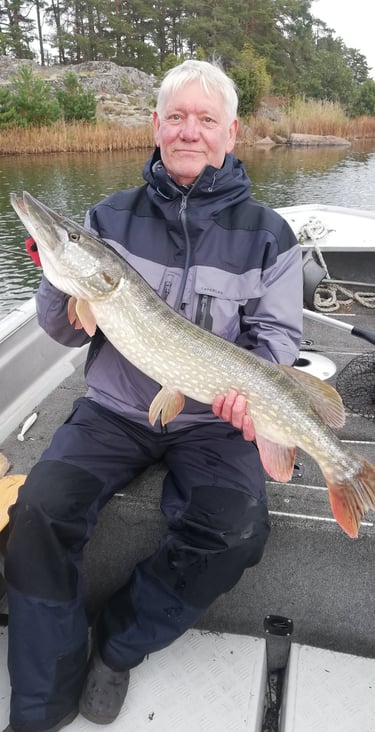 un homme est assis dans un bateau de pêche en suède, il a un beau brochet.