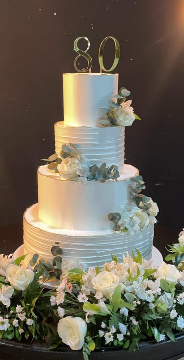 Bolo de aniversário decorado em camadas com flores brancas e verdes, celebrando 80 anos, ideal para