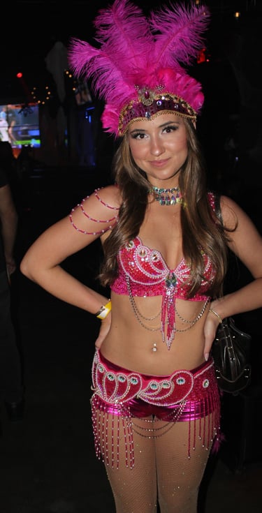 Woman wearing a vibrant pink showgirl costume with a feathered headpiece and beaded sequins.