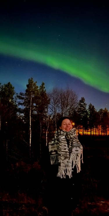 a woman standing under the northern lights with a smile