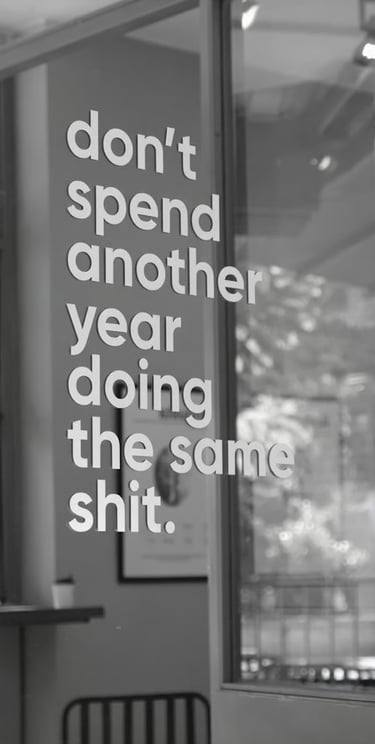 A phrase displayed in a store window that reads, “Don't spend another year doing the same s**t”