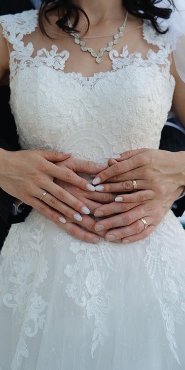 Close-up of bride and groom holding hands over the bride’s wedding dress during a wedding photoshoot