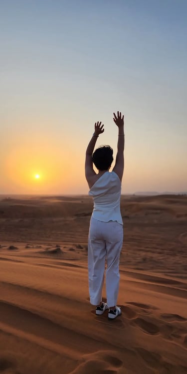 A person seen from behind in the desert with arms in the air facing the sunset