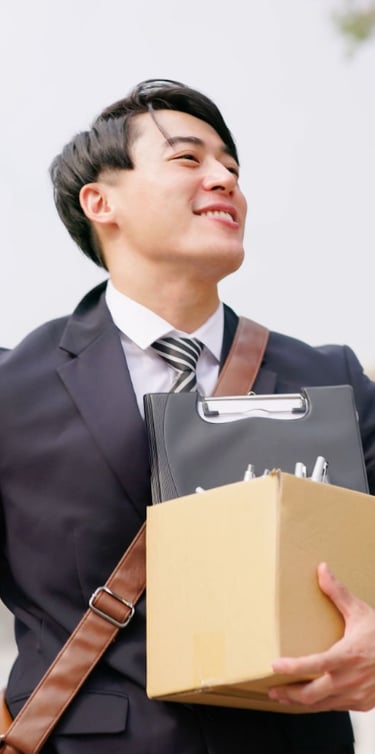 Homme souriant en costume portant un colis et un classeur.