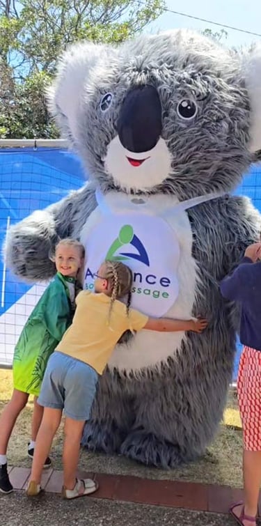 two children hugging a huge Advance Body Massage Koala Mascot
