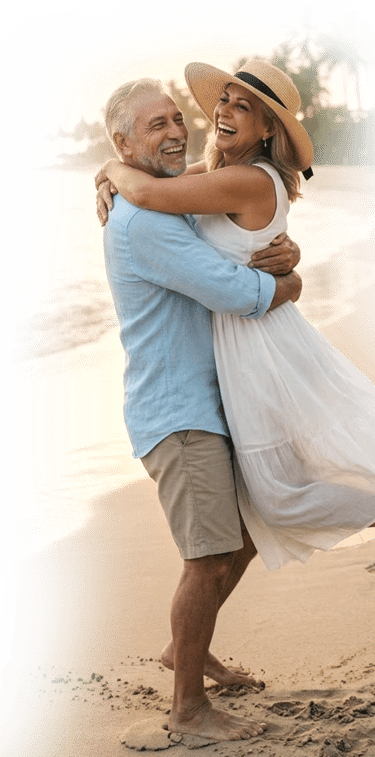 Happy senior couple hugging and laughing on a tropical beach during a romantic sunset vacation.