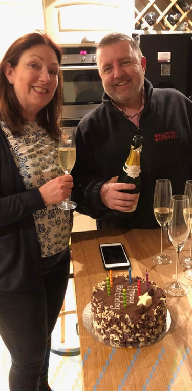 Two adults celebrating birthday in modern kitchen with champagne and cake reading 'Happy Birthday