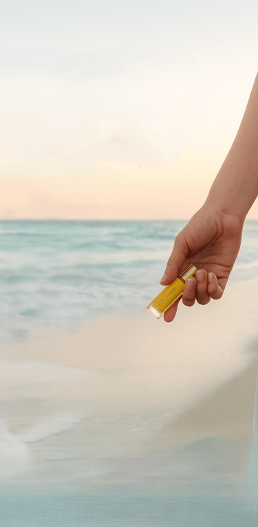 image of hand holding an essential oil bottle beachside