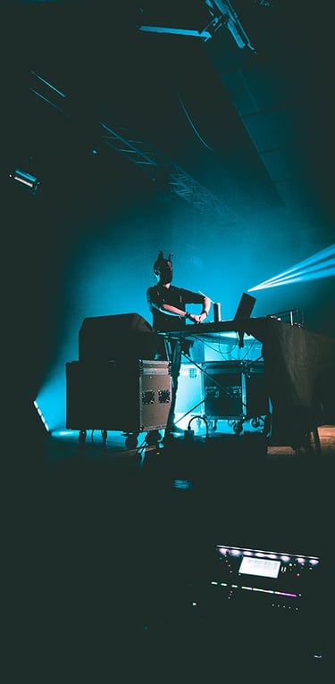 Vagues de lumières colorées projetées sur un DJ en pleine immersion dans son mix, capturées par Thomas Bordas.