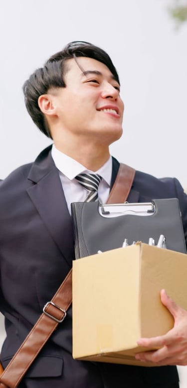 Homme souriant en costume portant un colis et un classeur.