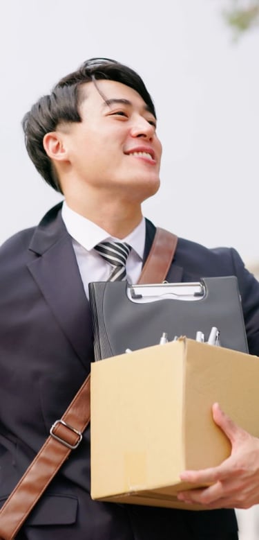 Homme souriant en costume portant un colis et un classeur.