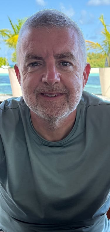 "Person seated at outdoor table in tropical resort with palm trees and lounge chairs nearby