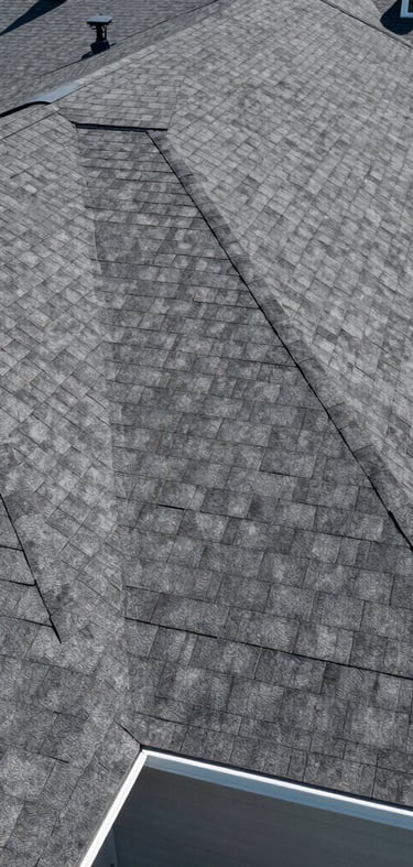 A clean drone shot of a newly completed residential roof with architectural shingles, bright daylight, flawless alignment, crisp gutter lines.