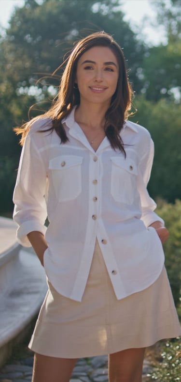 Smiling woman wearing a stylish white linen button-down shirt and beige skirt in a sunny park.