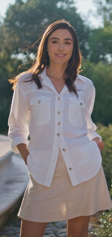 Smiling woman wearing a stylish white linen button-down shirt and beige skirt in a sunny park.