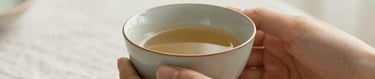 Close-up of hands holding a warm ceramic tea cup, soft natural light, linen tablecloth, peaceful and cozy atmosphere