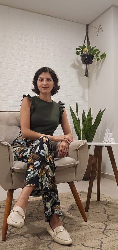 Woman in floral pants and olive top sitting in an armchair by a snake plant.