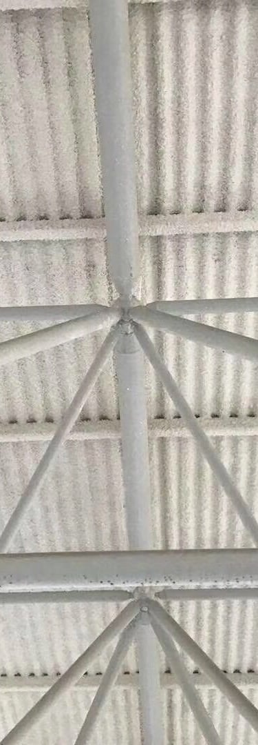 White industrial steel roof trusses supporting a corrugated metal ceiling with spray foam insulation.