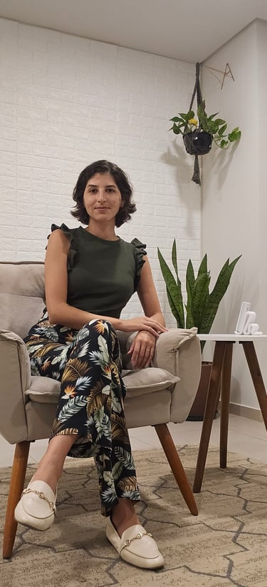 Woman in floral pants and olive top sitting in an armchair by a snake plant.