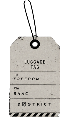 Vintage luggage tag with text 'To Freedom Via BHAC' and Dystrict logo on a dark background.