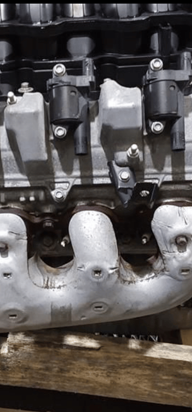 A high-performance V8 car engine with silver exhaust manifold and black ignition coils on a wooden pallet.
