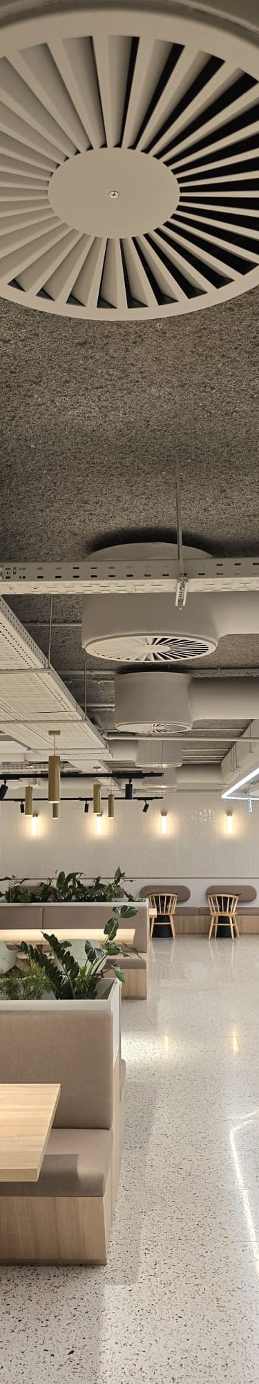 Modern office cafeteria with industrial exposed ceilings, white ventilation ducts, and comfortable booth seating.