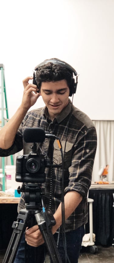 a man in a plaid shirt and headphones on a tripod recording video